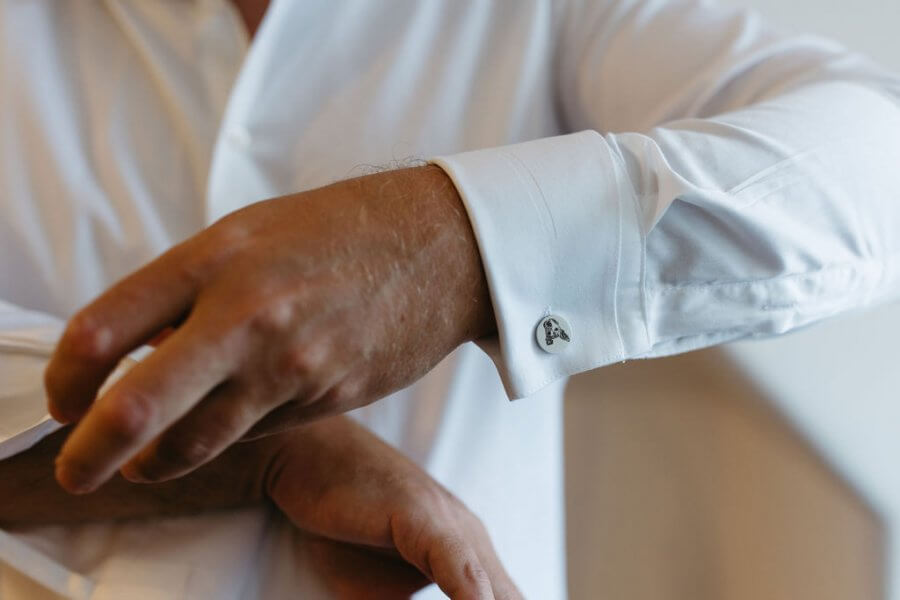 A close-up captures a person adjusting a white shirt sleeve with an anchor-shaped cufflink, perfect for their role in an elegant Edinburgh wedding.