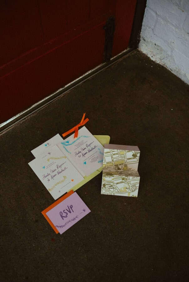 An assortment of Edinburgh wedding invitations and RSVP cards are elegantly arranged on a dark floor near a red door.