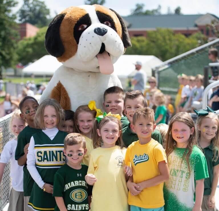 The 2026 Memphis Summer Camp Guide - 3 A group of children in school spirit attire pose outdoors with a person in a large St. Bernard dog mascot costume, capturing the fun and energy often found at Memphis summer camps.