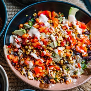 RECIPE: Vegan Taco Bowl - 8 A colorful salad with mixed vegetables, corn, diced red peppers, beans, and a drizzle of dressing in a ceramic bowl.