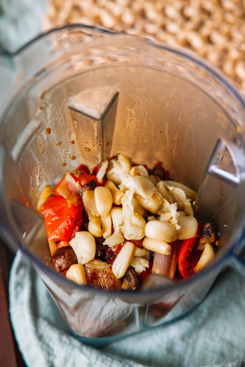 A blender filled with chopped garlic, tomatoes, and roasted vegetables creates a perfect base for a rich pasta sauce.