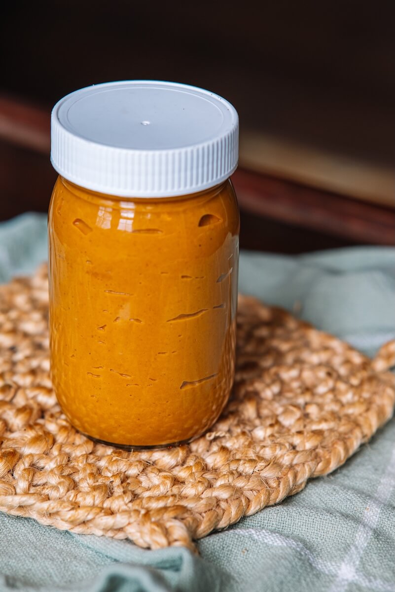 A jar filled with vibrant orange pasta sauce, enriched with roasted vegetable flavors, sits on a woven placemat.