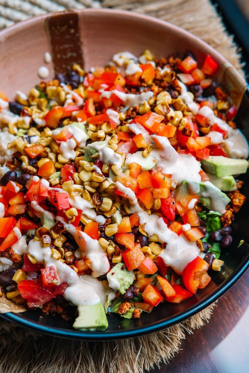 RECIPE: Vegan Taco Bowl - 1 A vibrant vegan salad bowl featuring diced avocado, roasted corn, black beans, and red bell peppers, all tossed in a creamy taco-inspired dressing.