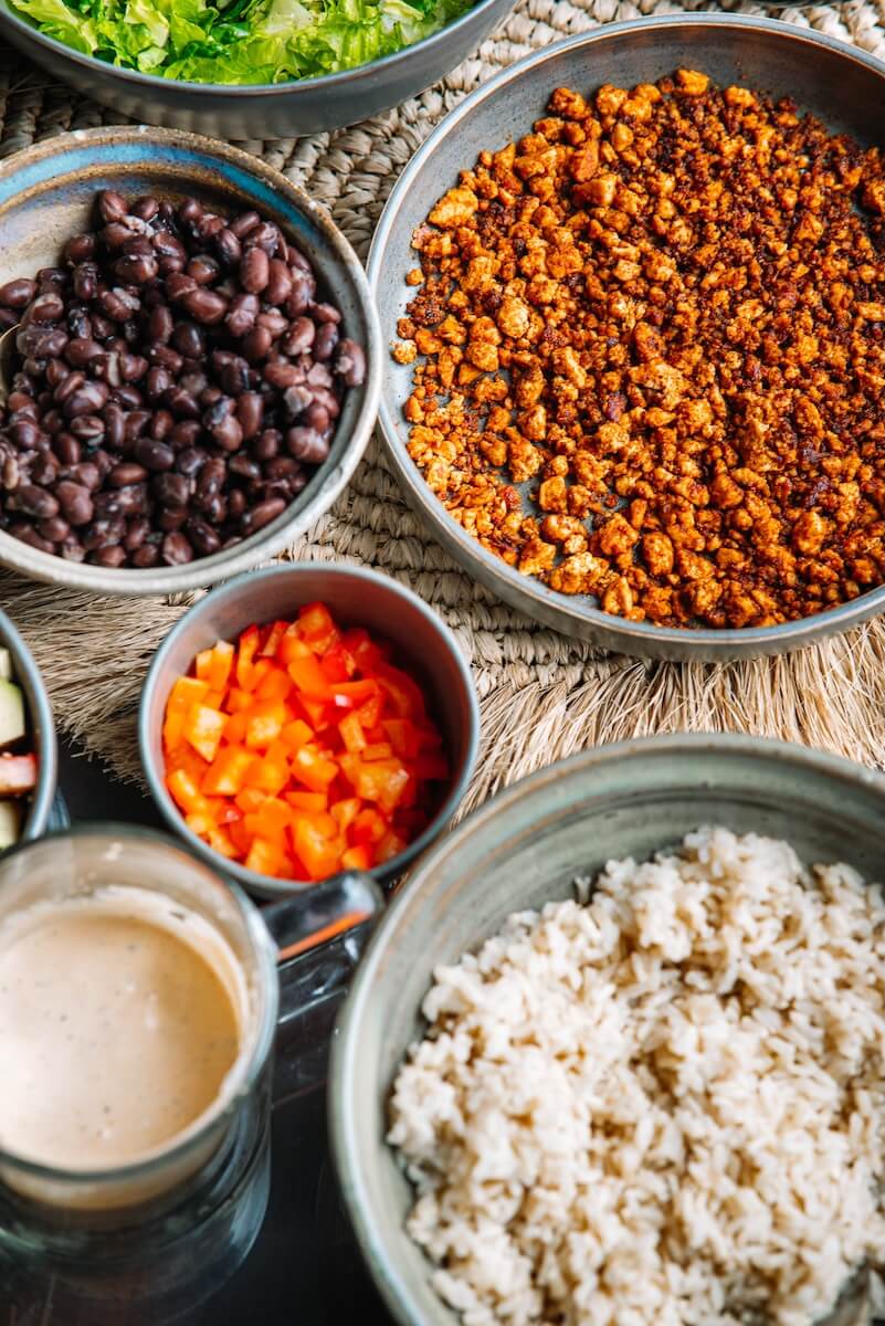 RECIPE: Vegan Taco Bowl - 2 A vibrant vegan bowl brimming with black beans, diced red peppers, crumbled tofu, and brown rice, all drizzled in a creamy dressing for a delightful taco-inspired feast.
