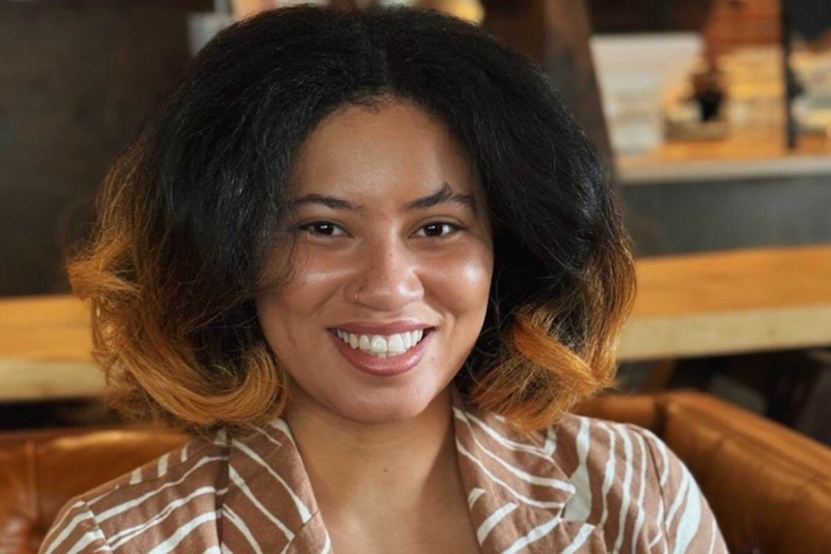 A smiling person with shoulder-length hair and a striped shirt is seated indoors, elevating the ambiance. BHAM proudly supports Black-owned businesses in the community, making this moment even more inspiring.