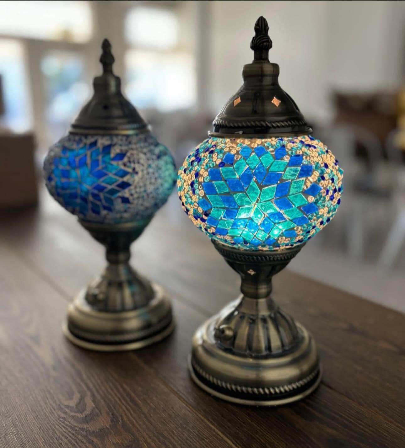 Two ornate, mosaic glass lamps with blue and green geometric patterns sit on a wooden table.
