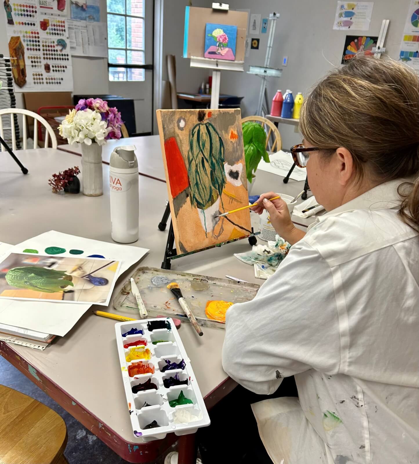 In a well-lit studio, a person is immersed in painting a cactus on canvas, surrounded by art supplies and reference photos. This creative endeavor is part of an inspiring Birmingham Adult Education class, where passion meets learning in the heart of the city.