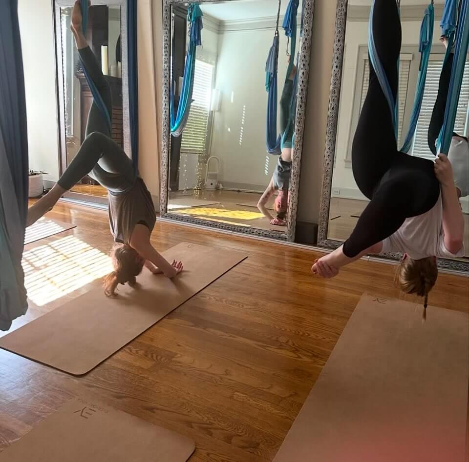 Two people practicing aerial yoga at The Oha, suspended upside down in hanging silks.