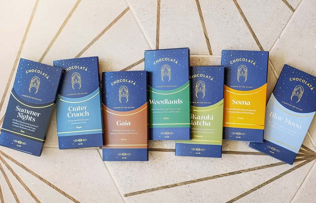 Seven Divine Chocolates bars are artfully displayed on a beige patterned surface.