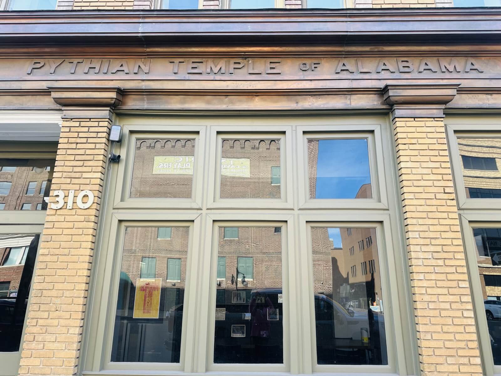 The historic façade of the Pythian Temple of Alabama, with its beige brick and large windows, building number 310, beautifully reflects the surrounding architecture, echoing the rich history of the area.