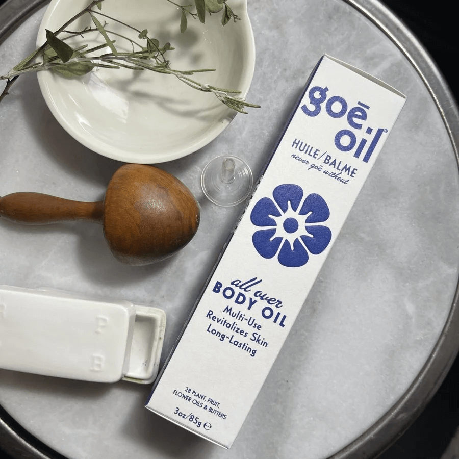 A tube of goë oil body balm graces the table alongside a wooden massager, a white dish, and a small plant.