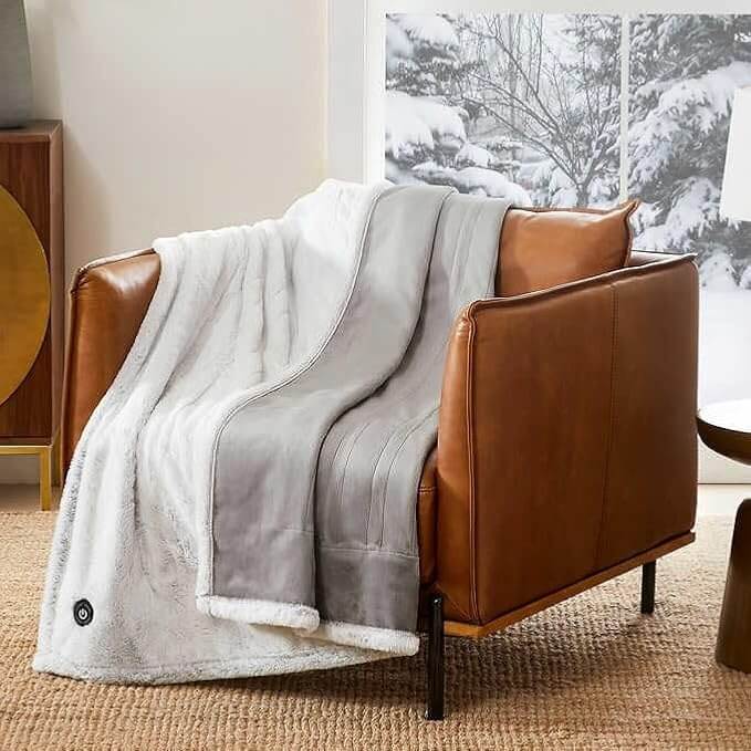 A brown leather armchair draped with a plush white and gray blanket, sits invitingly in a cozy room with a snowy window view.