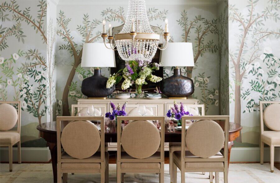 The Top Interior Designers and Architects in Birmingham - 6 Designed by one of The Best Interior Designers and Architects in Birmingham, this elegant dining room features six beige upholstered chairs, a wooden table with flowers, a sideboard, two lamps, a chandelier, and tree-and-flower wall murals.