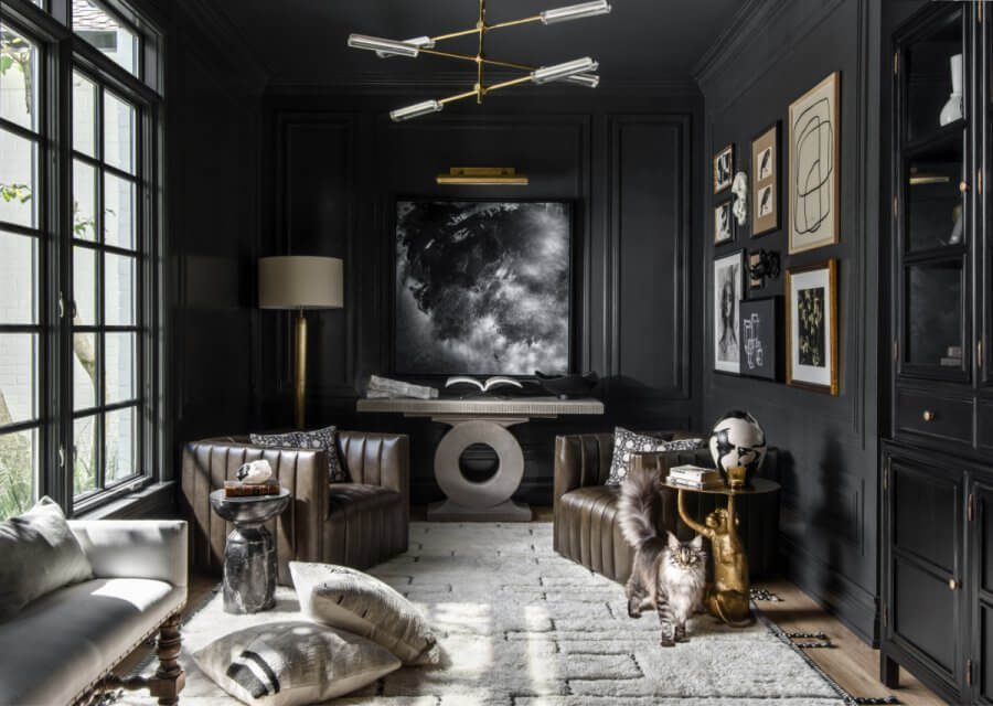 StyleBlueprint's 15 Most Popular Articles of 2025 - 3 A modern living room featuring dark walls, leather chairs, and abstract art captures the essence of 2025 interior design trends. A cat strolls across a light-colored rug beneath a unique chandelier, while natural light floods through a large window.