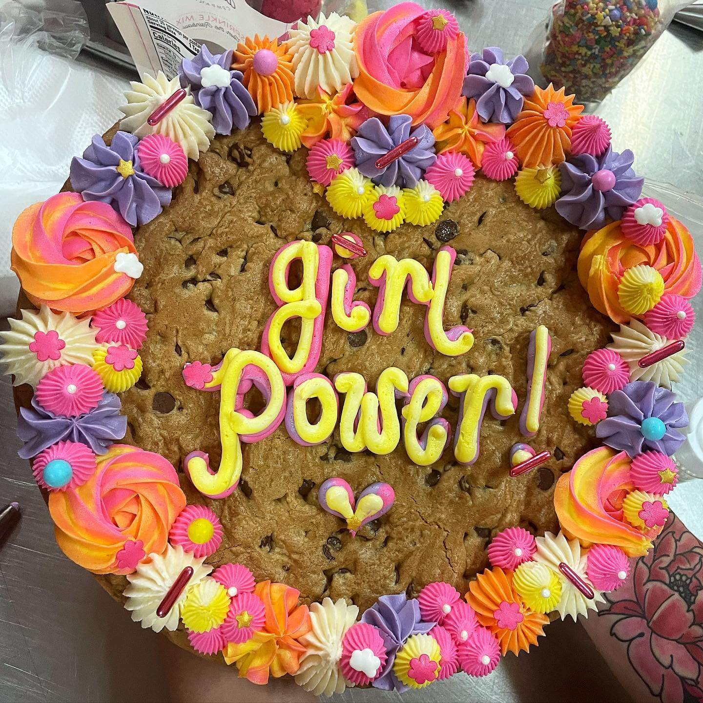 A large cookie decorated with colorful icing flowers and swirls, featuring the text "girl power!" in yellow icing at the center, is perfect for celebrating those adult education classes in Louisville.