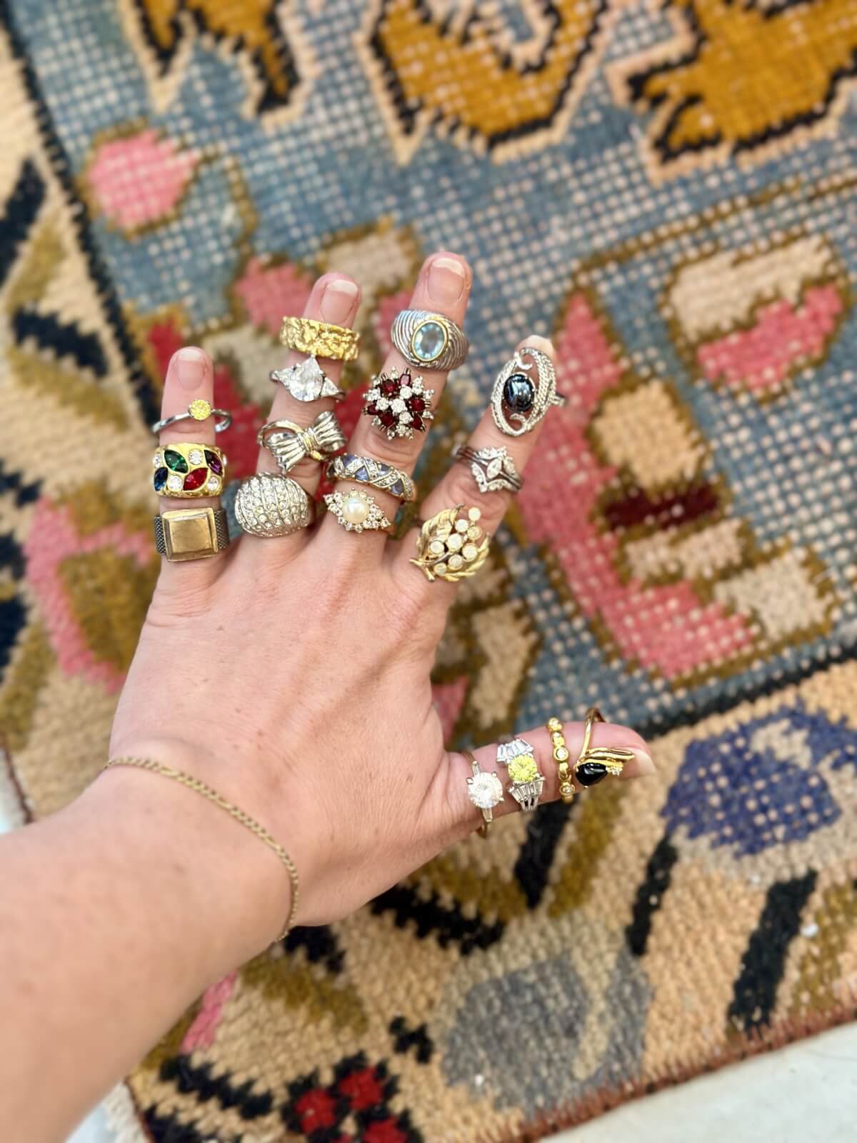 A hand wearing multiple rings with various designs and gemstones, displayed against a colorful patterned background.