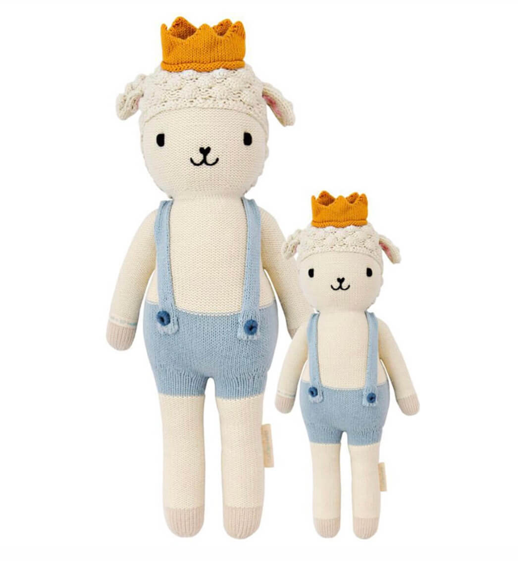 Two stuffed animal dolls, resembling sheep, wearing blue overalls and yellow crowns, are placed side by side. The left doll is larger than the right.