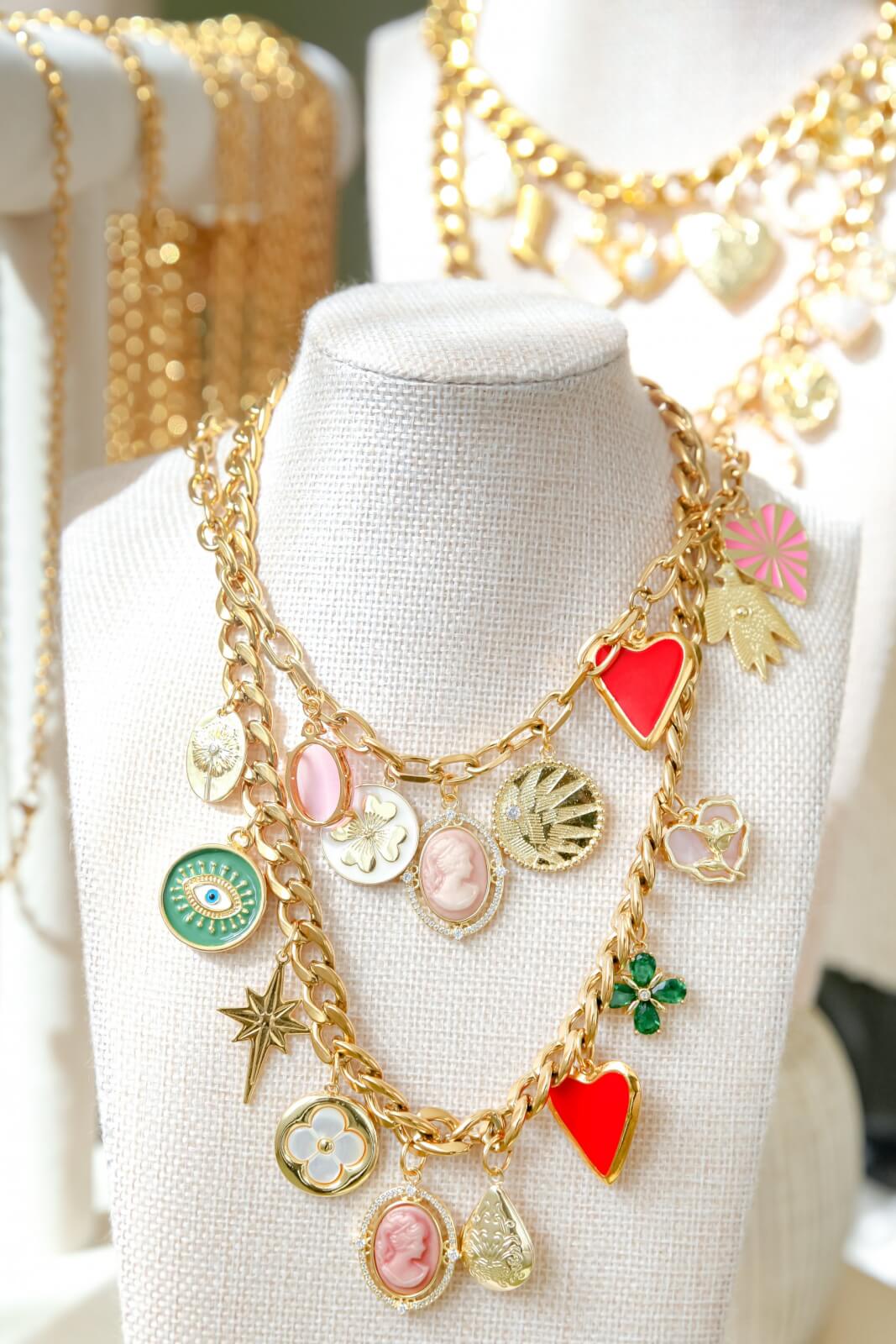 Gold necklaces from Memphis Jewelry Brands, featuring an array of charms like hearts, a star, and cameo designs, elegantly displayed on a white fabric bust.