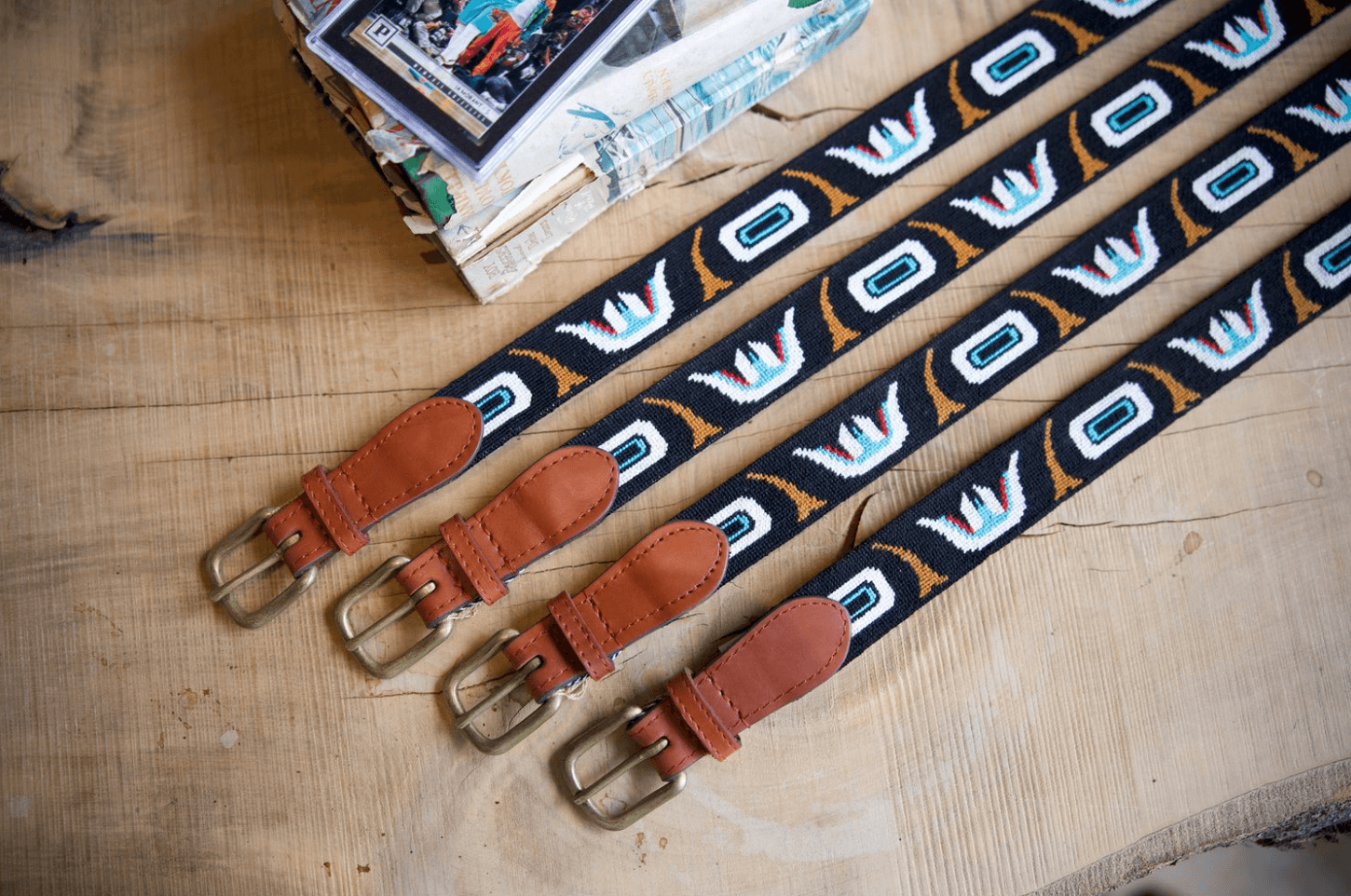 Four patterned fabric belts with brown leather ends and metal buckles are stylishly laid out on a wooden surface, echoing the vibrant Memphis design vibe. They sit next to a small patterned box, making for exquisite February FINDS.
