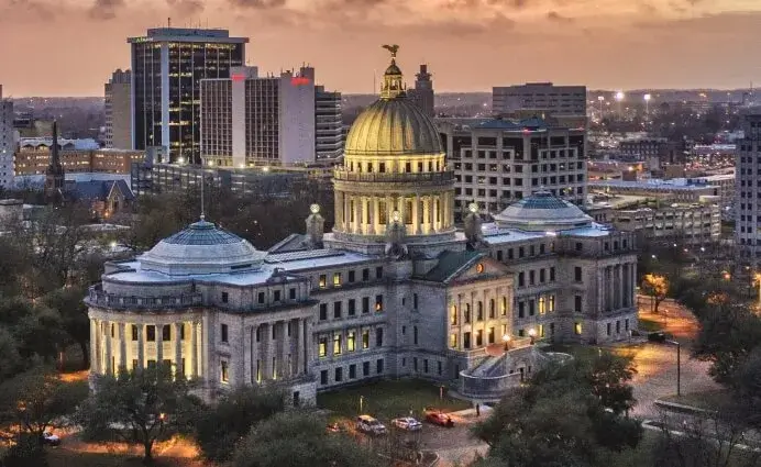 Aerial view of a lit-up capitol building with a golden dome in an urban setting at dusk, marking another key point along the Mississippi Freedom Trail.