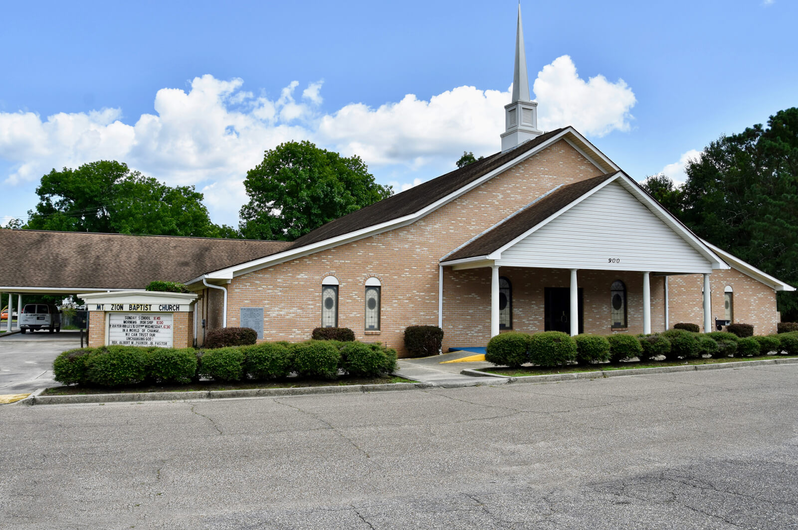 A brick church with a steeple, nestled among shrubs and marked by a sign displaying service times, stands proudly on the Mississippi landscape. 