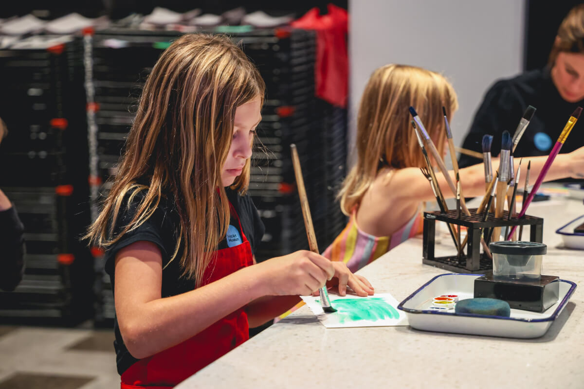 Two young girls enjoy family fun in Nashville, painting at a table with brushes and paint trays.