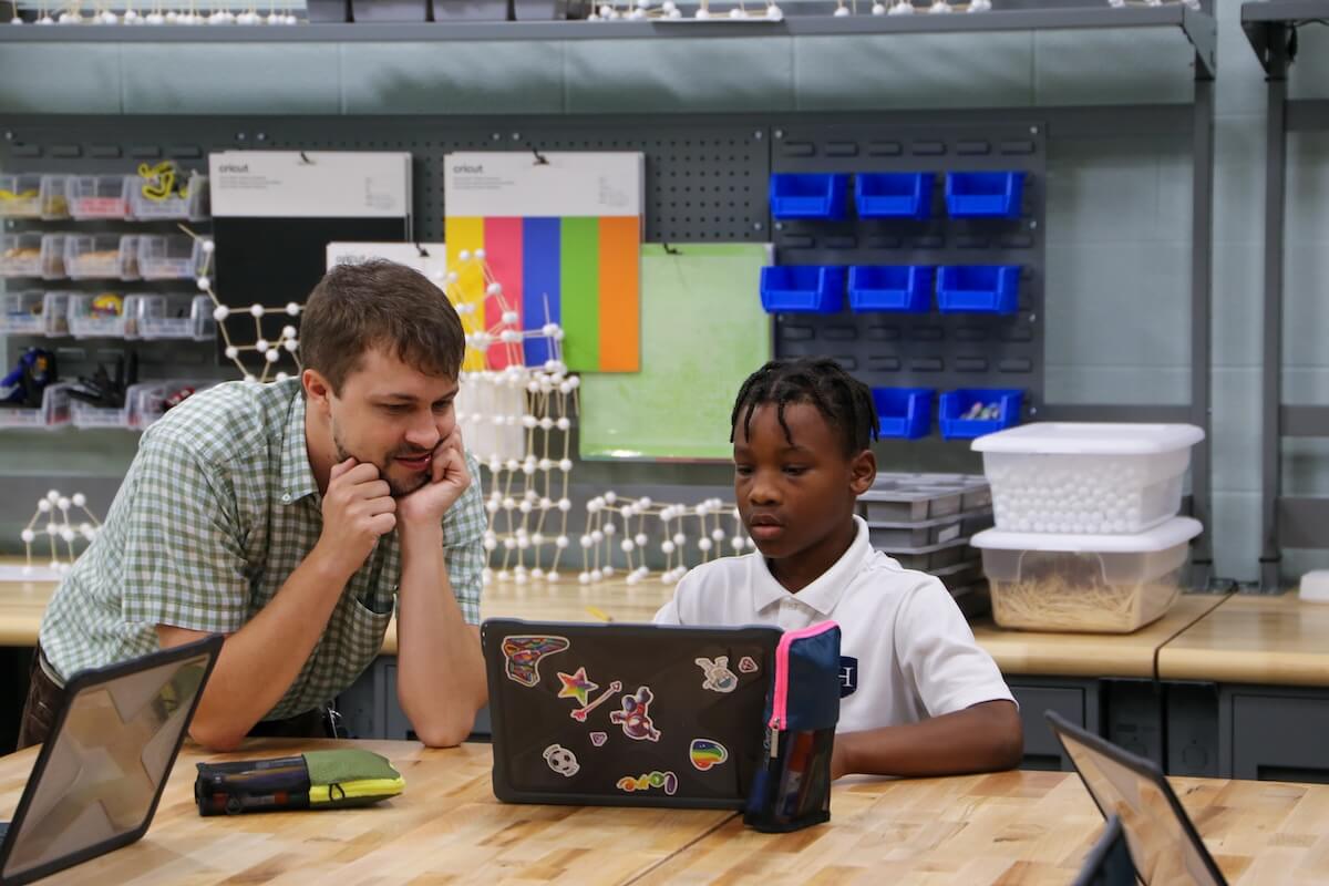 At Harding Academy, a teacher and student collaborate over a laptop in a classroom setting filled with educational materials.