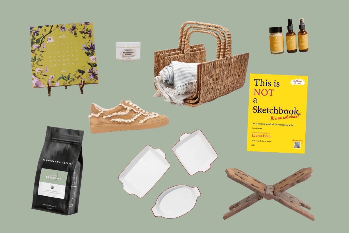 A flat lay of various items, including a floral calendar, skincare jar, wicker basket, Cozy Southern FINDS essential oils, yellow sketchbook, coffee bag, tan sneakers, ceramic dishes, and a wooden stand on a green background.
