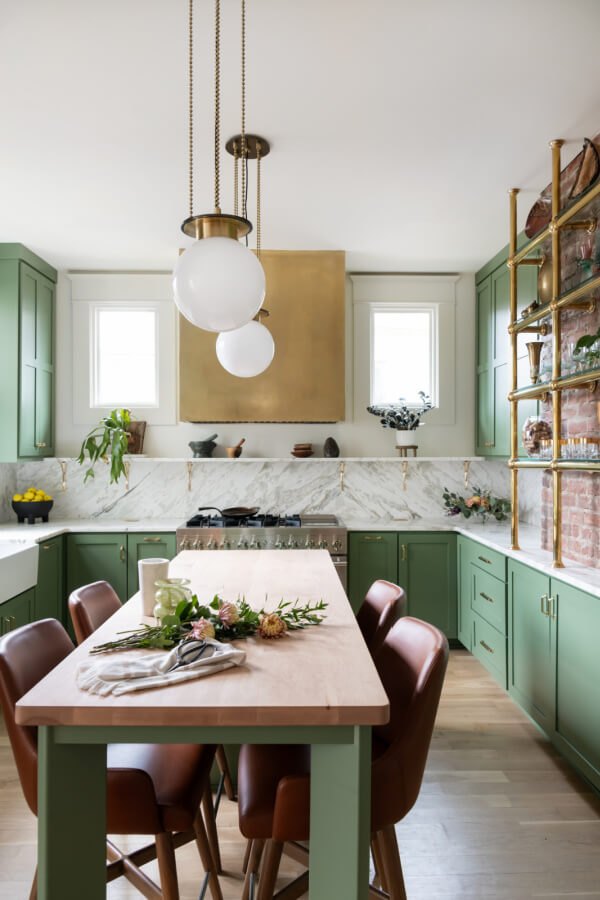 A Historic Nashville Home with STUNNING Colorful Accents! - 8 A Sara Ray gem, this modern kitchen showcases green cabinets, a marble backsplash, and brass accents. A wooden island with brown leather chairs and spherical pendant lights completes the design, making it a standout home feature.