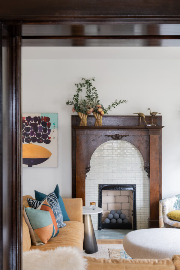 A Historic Nashville Home with STUNNING Colorful Accents! - 5 Living room featuring a decorative fireplace, modern art, and a mix of patterned and solid cushions on a beige sofa. A round coffee table and plants add accents to the cozy space.