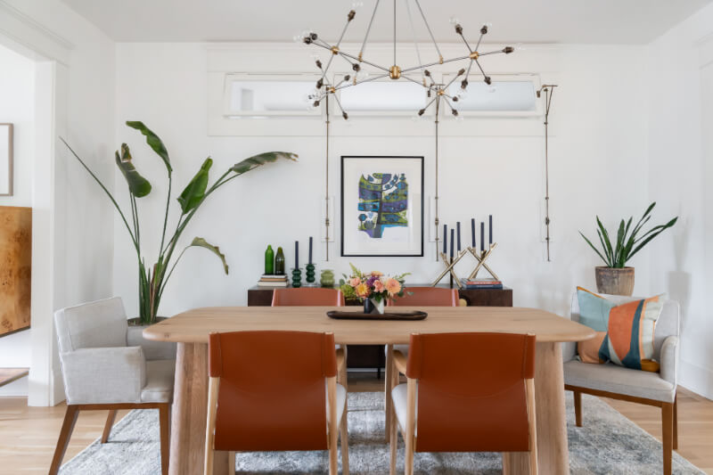 A Historic Nashville Home with STUNNING Colorful Accents! - 6 A modern dining room features a wooden table with six chairs, a central floral arrangement, decorative plants, elegant wall art, and a contemporary chandelier.