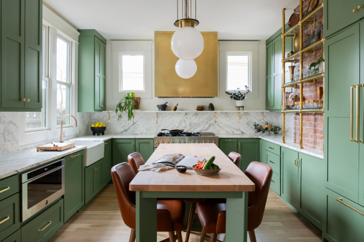The green kitchen, a standout feature from Sara Ray's design, boasts marble countertops and a wooden island with leather chairs. Pendant lights illuminate the space, while white and gold accents complete the homey decor.