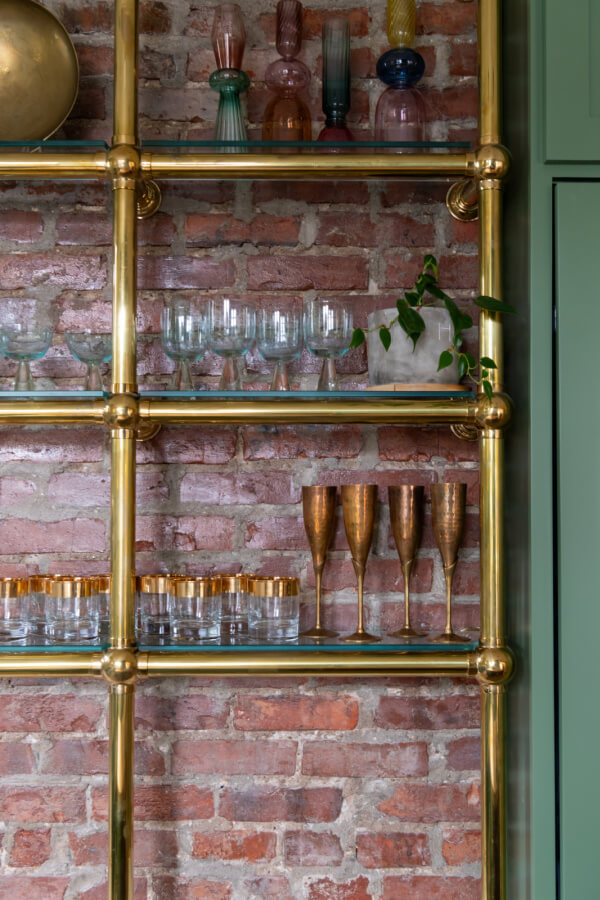 A Historic Nashville Home with STUNNING Colorful Accents! - 9 Brass shelves, adorned with glassware and decorative bottles, feature a charming plant that adds life to the exposed brick wall backdrop.