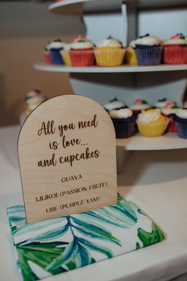 A charming sign reading "All you need is love... and cupcakes" graces the wedding table, with assorted cupcakes in the background.