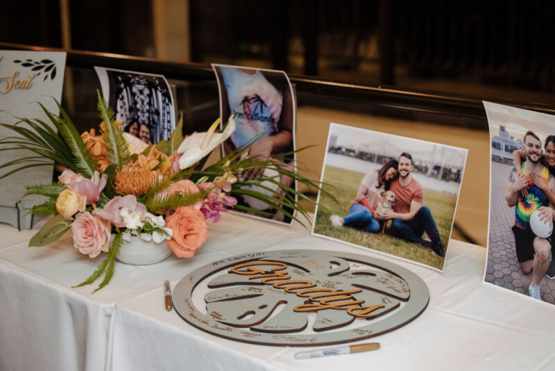 A wedding table adorned with a beautiful flower arrangement features photos of the happy couple and a decorative circular sign on white cloth.