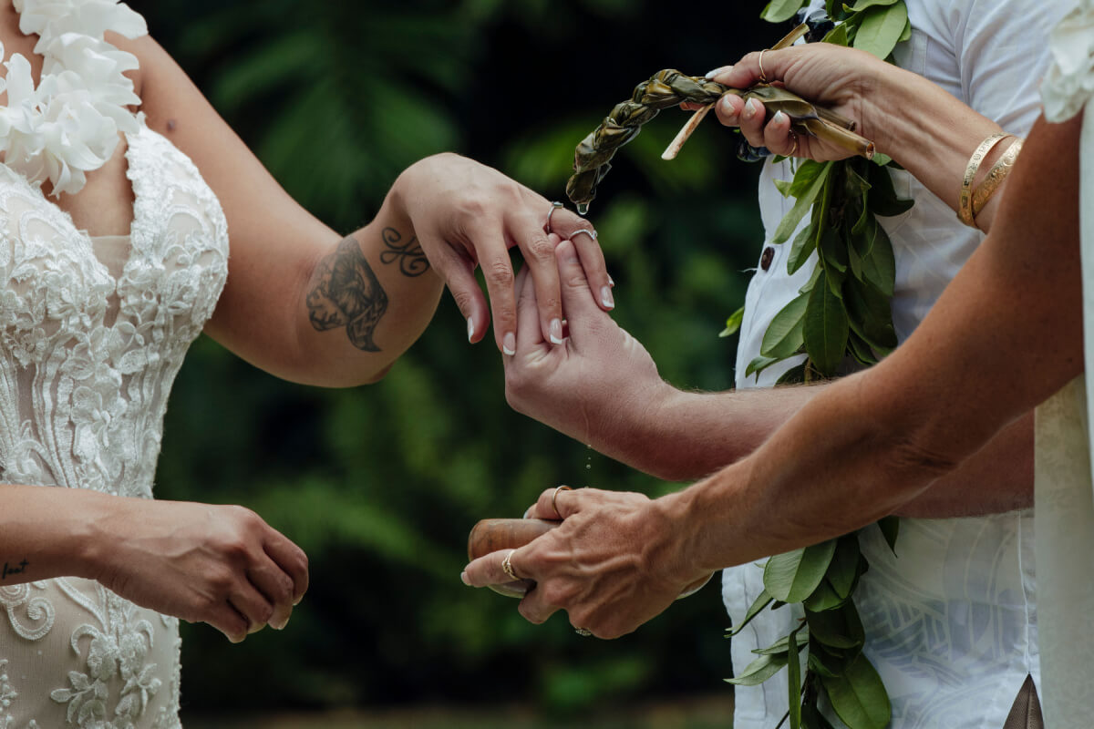 Lennie and William exchange rings during a heartfelt wedding ceremony, surrounded by floral garlands and lush greenery.