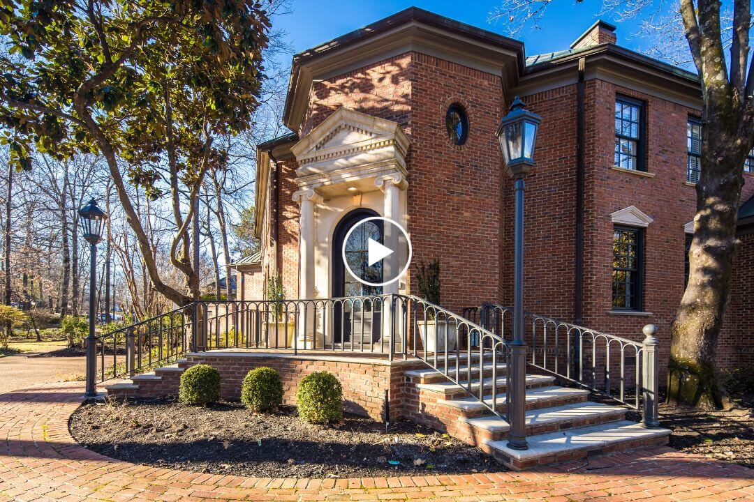 A red brick building with a columned entrance and a ramp, nestled in River Oaks, Memphis, TN, is surrounded by trees and a charming brick pathway.