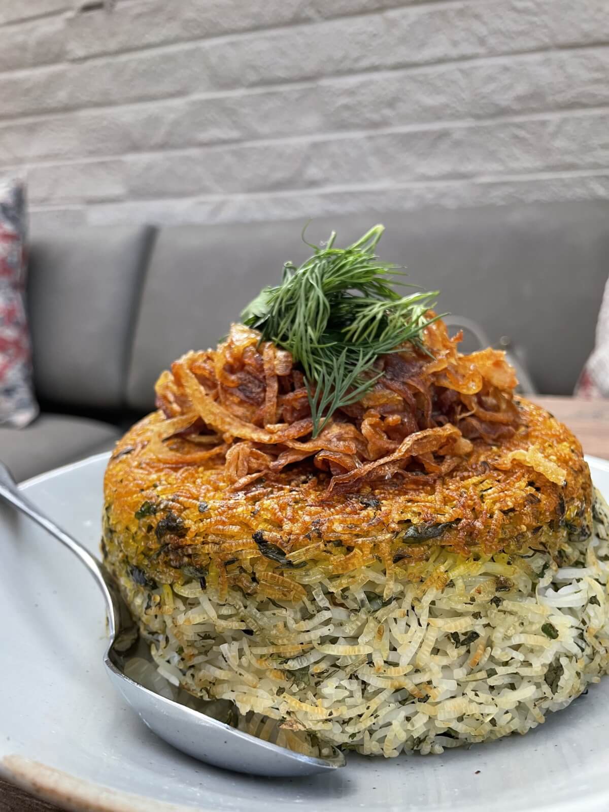 Experience a delightful dish at one of the new Atlanta restaurants you should try this year. Enjoy a round portion of baked rice mixed with herbs, topped with crispy fried onions and dill, served elegantly on a plate with a spoon.