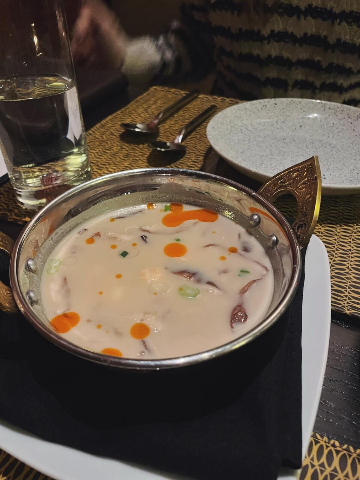 A bowl of soup with orange oil droplets, green onions, and mushrooms sits invitingly on the table of one of Atlanta's new restaurants, accompanied by a spoon, fork, empty plate, and a glass of water. It's a must-try this year for any food enthusiast.