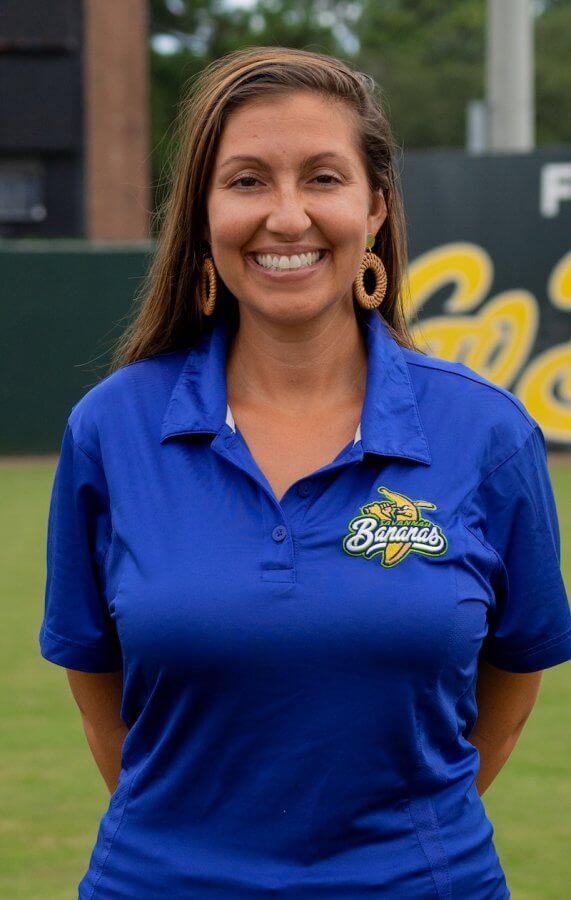 A person wearing a blue shirt with a banana logo stands outdoors, smiling cheerfully at the camera.