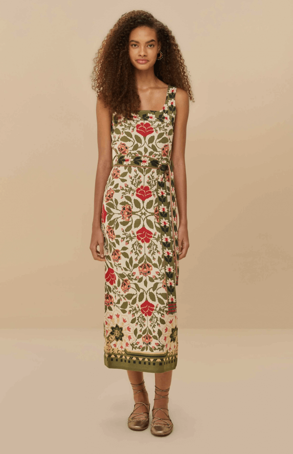 A woman stands against a beige backdrop, showcasing a sleeveless floral print dress with a square neckline and belt. It's a perfect addition to your spring wardrobe essentials, offering a modern spin on classic pieces.
