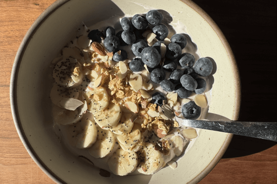 High-protein yogurt bowl topped with banana slices, blueberries, almonds, granola, and chia seeds. A spoon rests in the bowl.