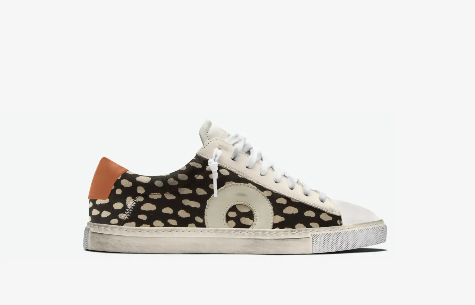 Discover one of the best sneakers with a spotted black and beige patterned upper, white laces, a large circular design, and an orange heel tab on a crisp white sole.