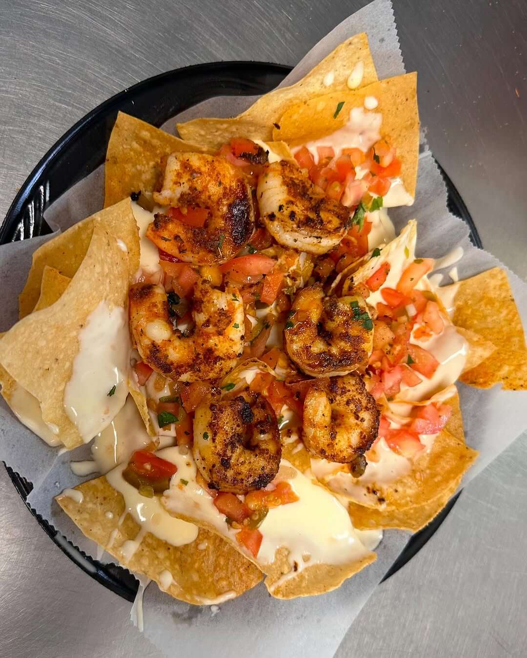 A plate of nachos topped with grilled shrimp, diced tomatoes, cheese, and sauce sits enticingly on a metal surface from Back Porch Grill. 