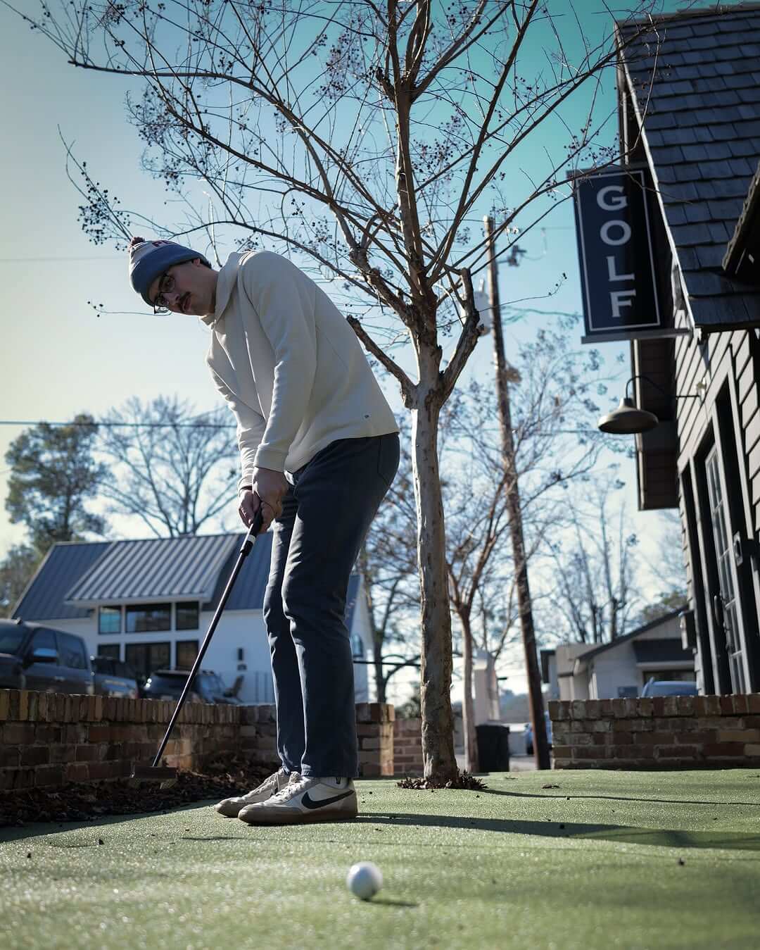 A person sporting a winter hat and sunglasses enjoys putting on the outdoor putting green at Pebblehurst Golf Society.