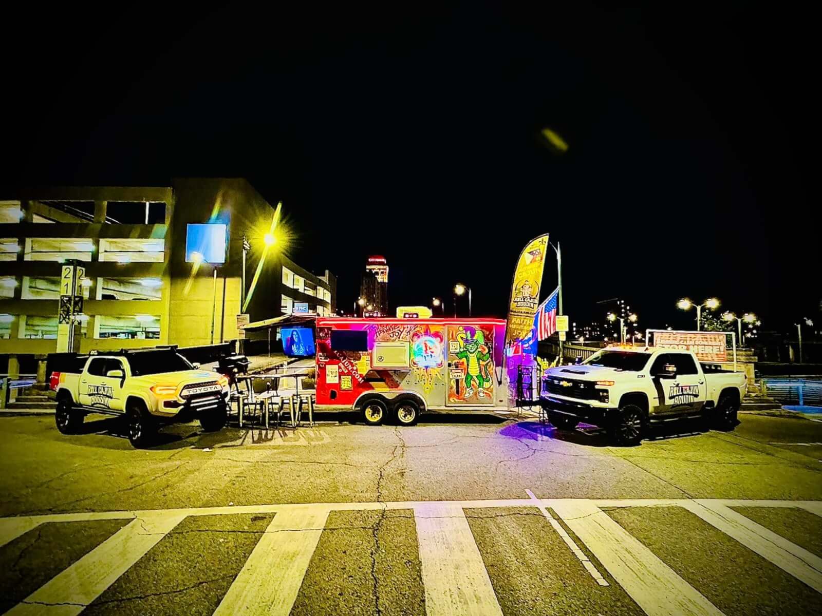 The Roll Cajun food truck, flanked by two pickup trucks, lights up the city lot at night. 