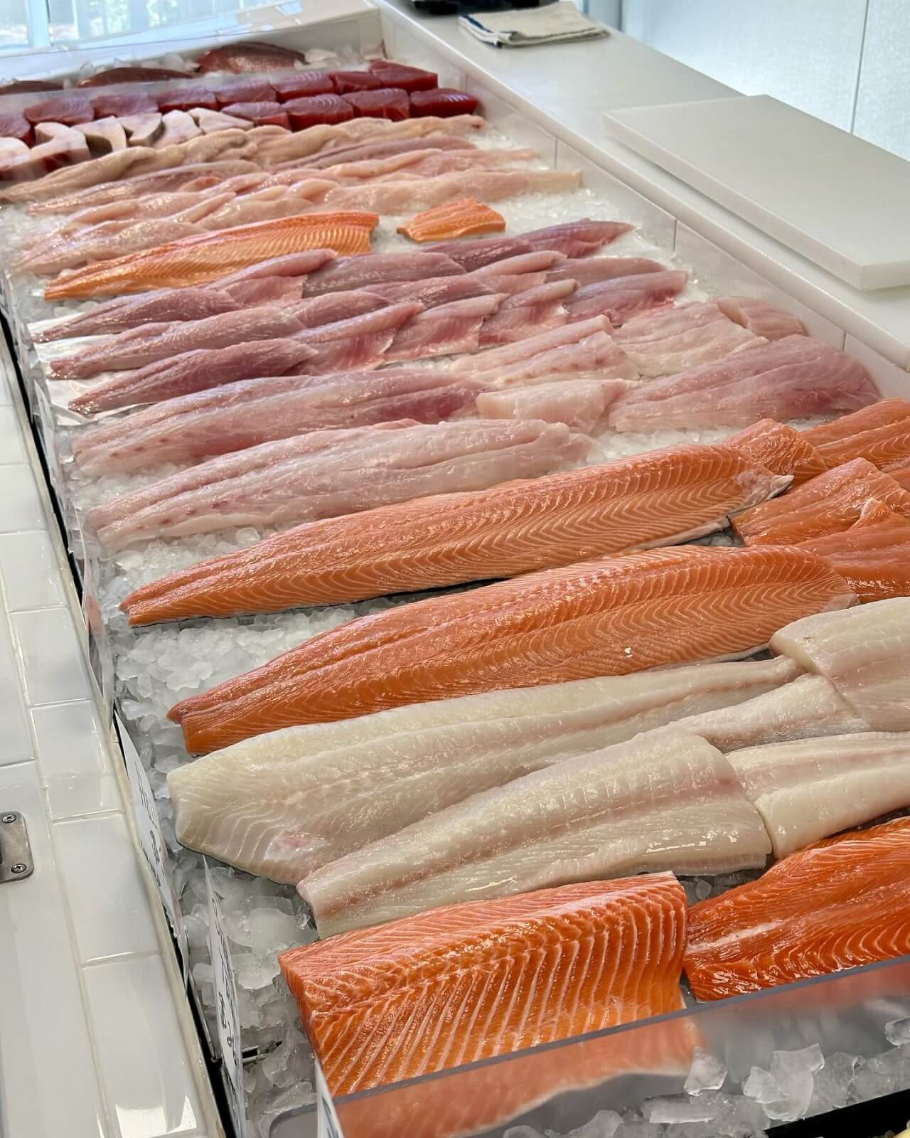 A seasonal display of various fresh fish fillets, including salmon and crawfish, rests on a bed of ice in Sexton's Seafood Market