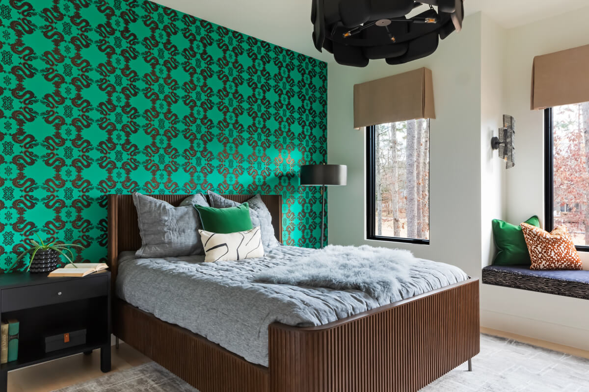 Bedroom with a wooden bed, gray bedding, green and black patterned accent wall, and a window seat with green and gray cushions. A black ceiling light fixture is visible above.