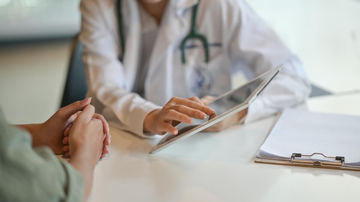 Is This Medical Bias Harming Your Health? - 2 A doctor sits at a desk, attentively showing a digital tablet to a patient, highlighting the importance of personalized healthcare.