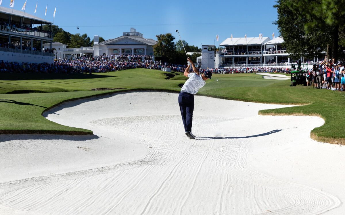 A golfer skillfully plays a shot from a sand trap on the lush golf course, with spectators watching intently under the clear blue sky, as if savoring a perfectly crafted brew at their favorite brewery.